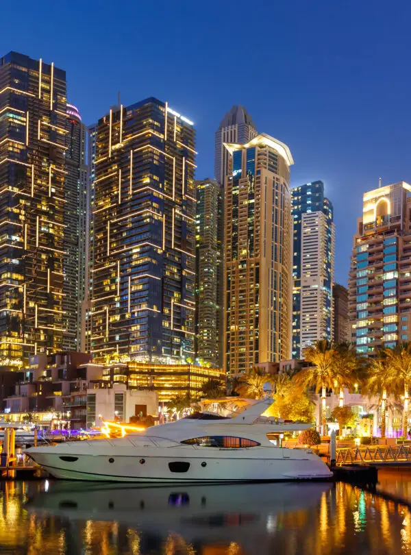 Dubai Marina and Harbour skyline architecture wealth luxury travel with yacht boat at night panorama in United Arab Emirates